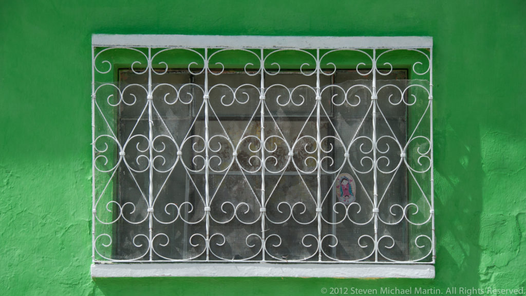 White decorative iron window grille with curling scrollwork set into a bright green wall in Flores, Guatemala.