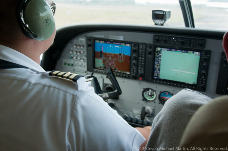 Pilot seated at the controls of a small aircraft with bright electronic cockpit displays.