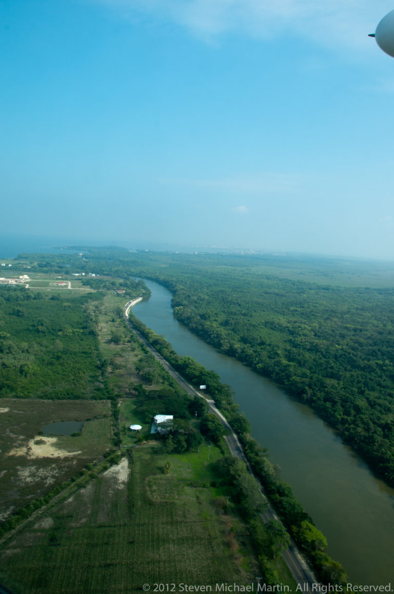 Winding dark waterway through flat green coastal vegetation, with a road and scattered clearings.