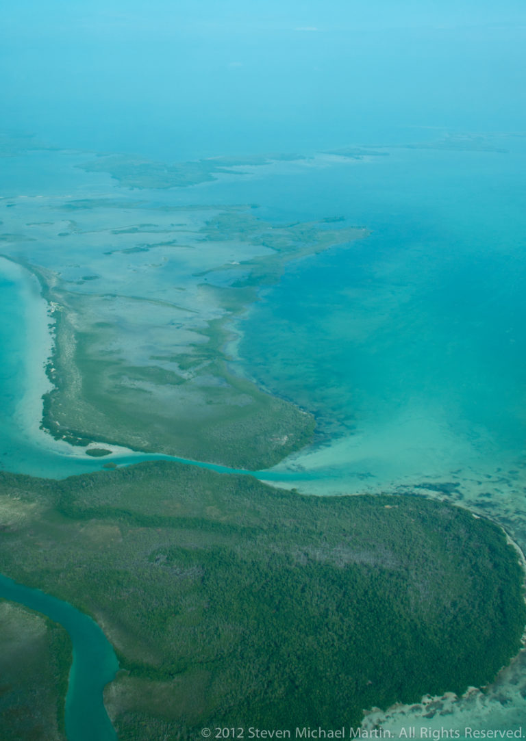 Mangrove-covered Belizean caye bordered by winding channels and broad pale turquoise shallows.