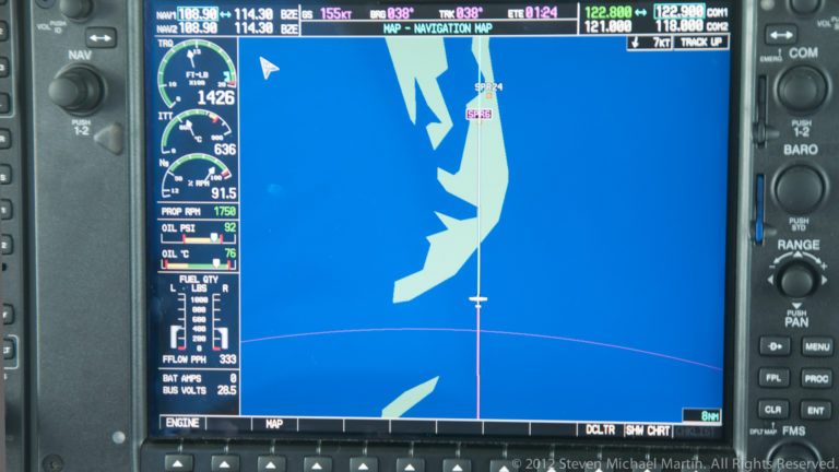 Aircraft moving-map navigation display showing coastal shapes, route line, flight data, and an aircraft symbol.
