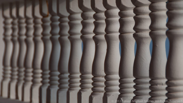 Close view of repeating white turned balusters receding along a veranda or balcony in San Pedro.