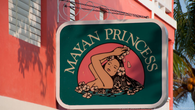 Green Mayan Princess business sign with cream lettering and an illustrated reclining woman against a coral wall.