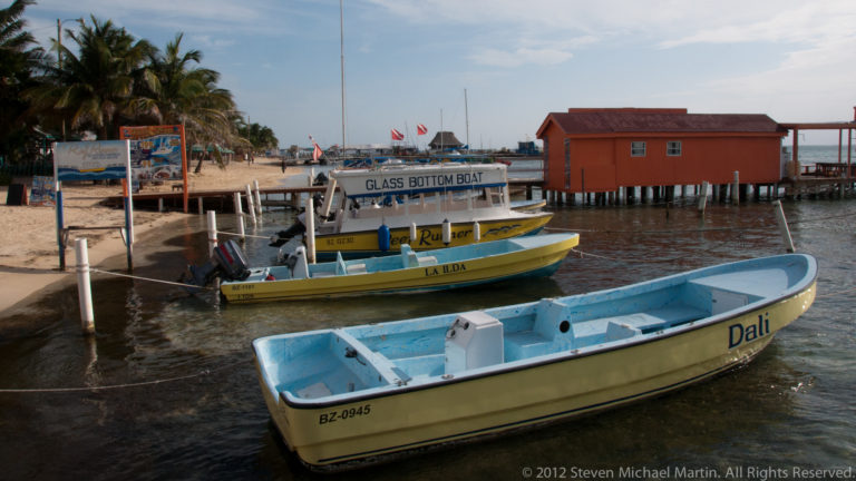 Colorful glass-bottom tour boat and small skiff moored beside wooden docks on the San Pedro waterfront.