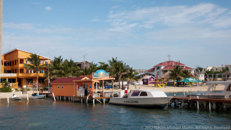 Passenger boat tied to a wooden dock beside colorful buildings and palms on San Pedro’s waterfront.