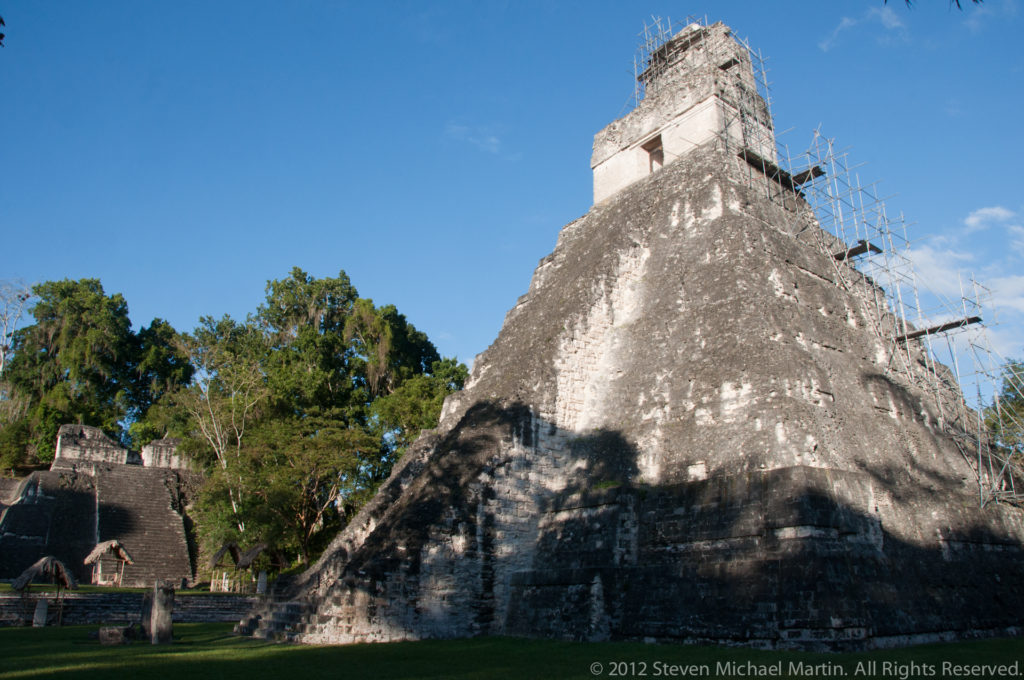 Wide oblique view of a steep Maya temple pyramid at Tikal, likely Temple II, with scaffolding around the upper temple and roof comb.