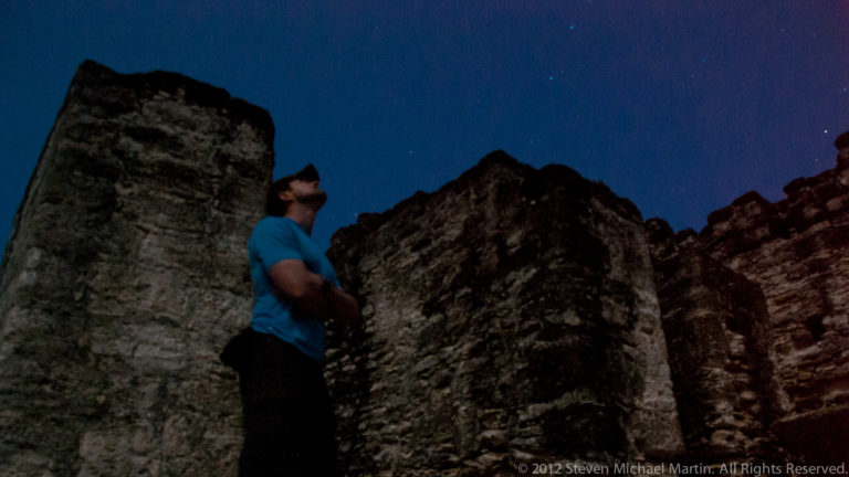Man standing beside tall Maya ruin walls at night beneath a star-filled sky.