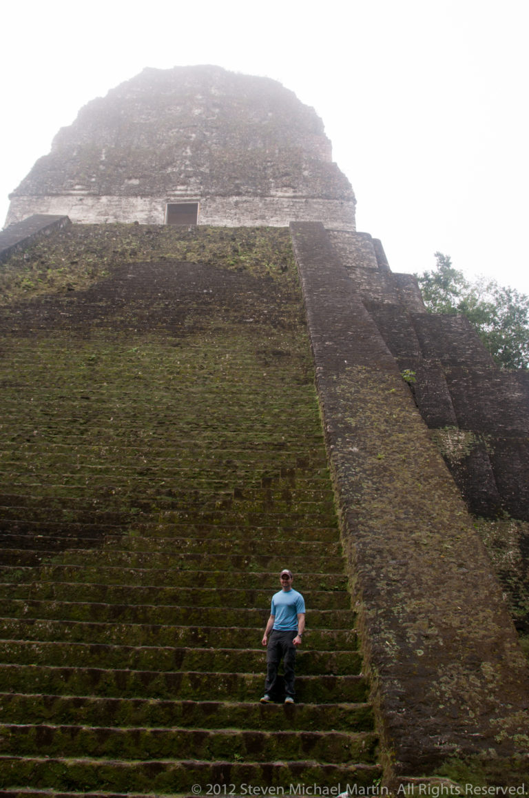 Close frontal view of a broad, steep Maya pyramid staircase at Tikal, with weathered limestone steps and moss-covered stone blocks.