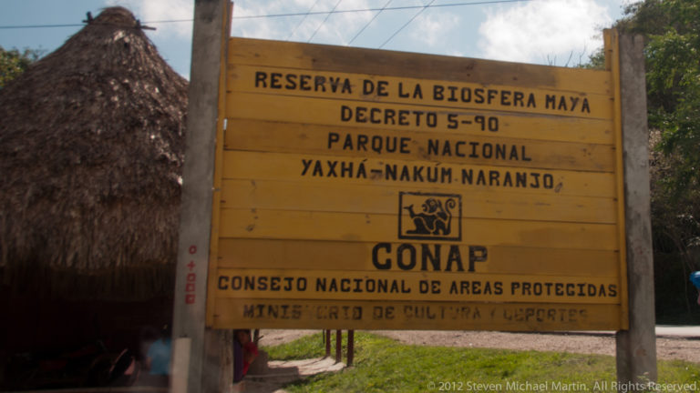 Wooden sign reading Reserva de la Biosfera Maya and Parque Nacional Yaxhá-Nakum-Naranjo with CONAP below.