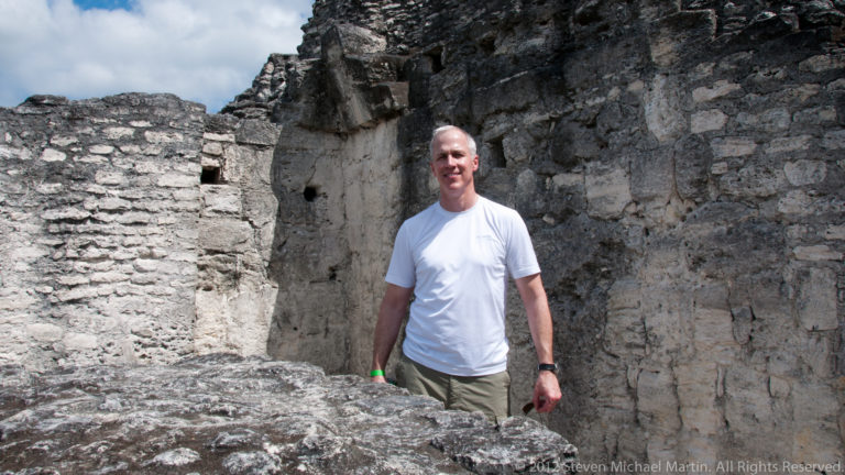 Visitor standing inside a roofless Maya stone chamber with thick weathered masonry walls at Yaxha.