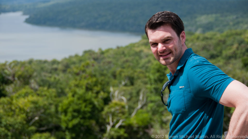 Visitor at a high viewpoint above tropical forest with Lake Yaxha visible in the background.