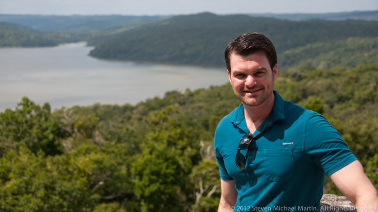 Close portrait of a visitor with Lake Yaxha and forest blurred in the background.