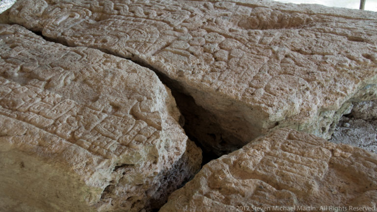 Close-up of weathered carved limestone blocks with shallow geometric and curving relief designs.