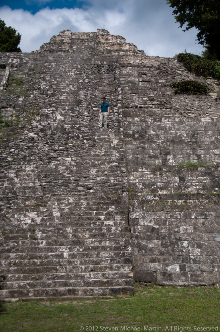 Small figure climbing the steep central stairway of a massive stone pyramid at Yaxha.