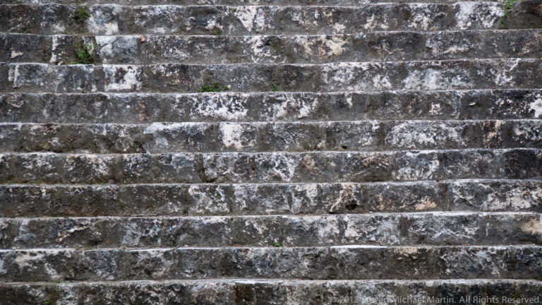 Close-up of weathered gray stone steps forming tightly spaced horizontal courses on a Maya structure.