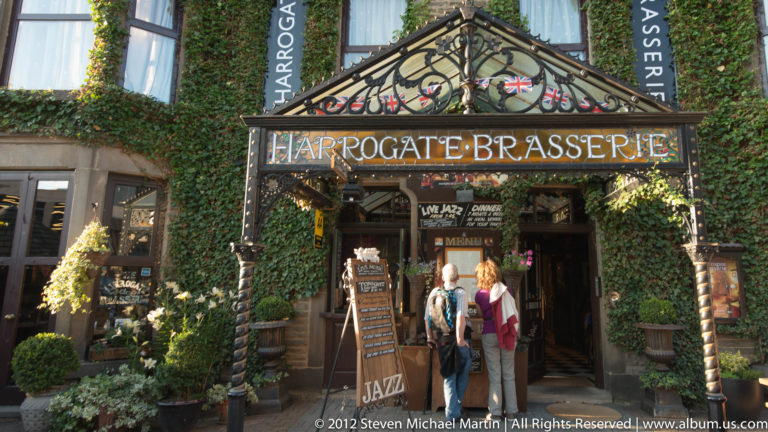 Two visitors stand beneath the ivy-covered canopy and sign at the entrance to the Harrogate Brasserie.