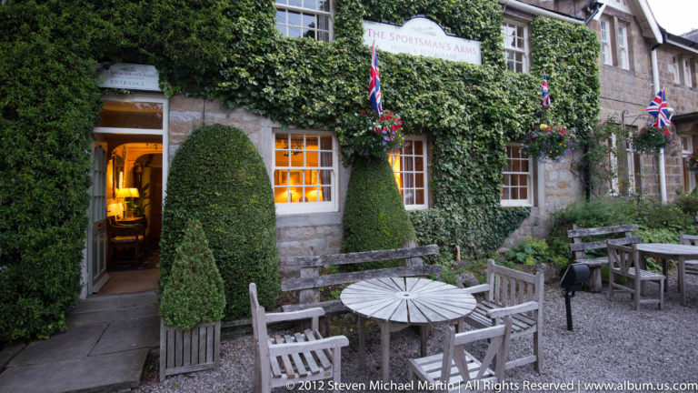 White café tables sit outside the ivy-covered Sportsman’s Arms, beneath hanging flowers and small British flags.
