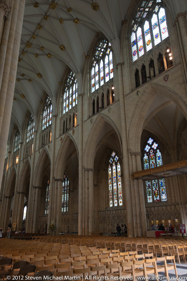 Stone arches and piers rise toward high stained-glass windows in a vaulted church interior.