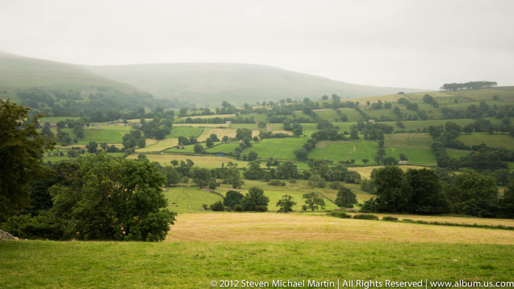 Hedged green and yellow fields form a patchwork across rolling hills fading into haze.
