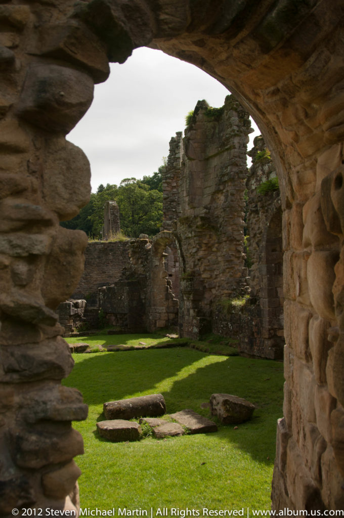 A low stone doorway frames green lawn and ruined masonry at Fountains Abbey.