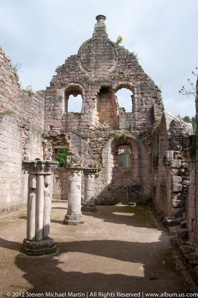 A roofless stone gable with arched openings stands within Fountains Abbey.