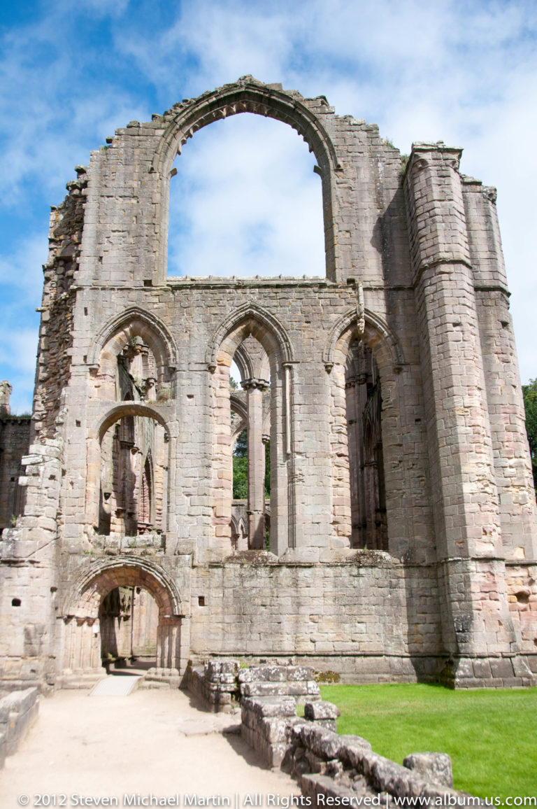 A roofless abbey façade has a broad upper arch and rows of smaller openings.