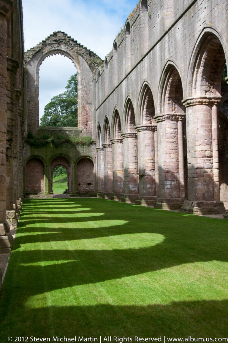 The green cloister garth is bordered by Fountains Abbey’s repeated stone arches.