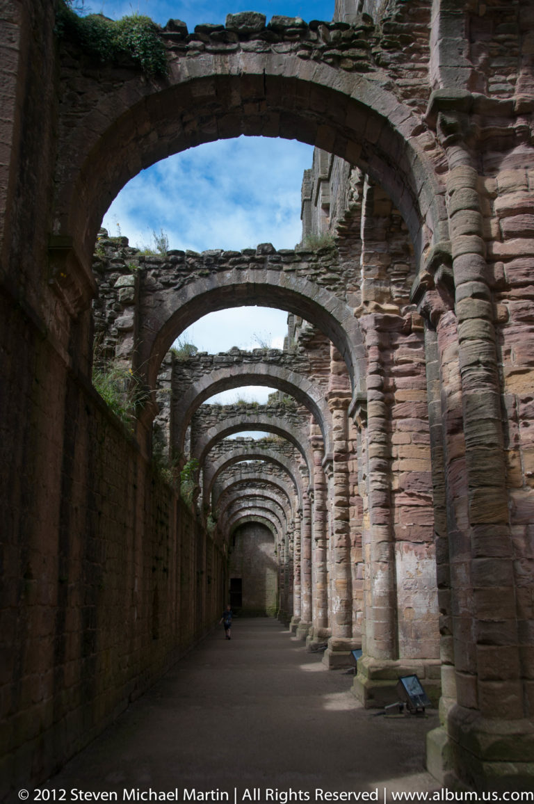 Nested stone arches recede through a shadowed cloister passage.