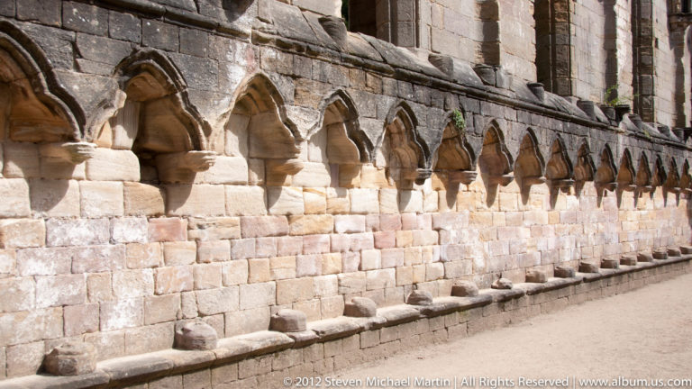 Carved stone capitals and small arches repeat along an abbey wall.