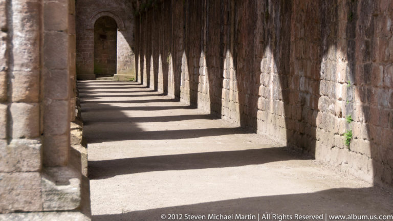 Sunlight and long shadows cross the repeating bays of a stone cloister.