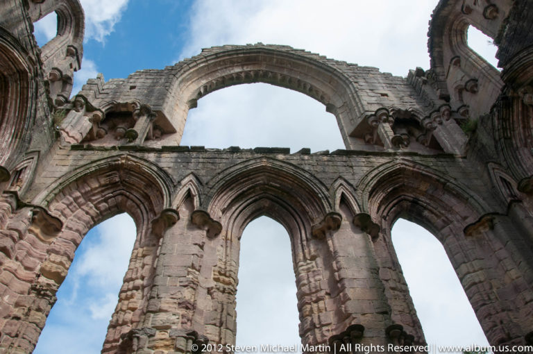A high stone arch and adjoining ruined walls are viewed from below.