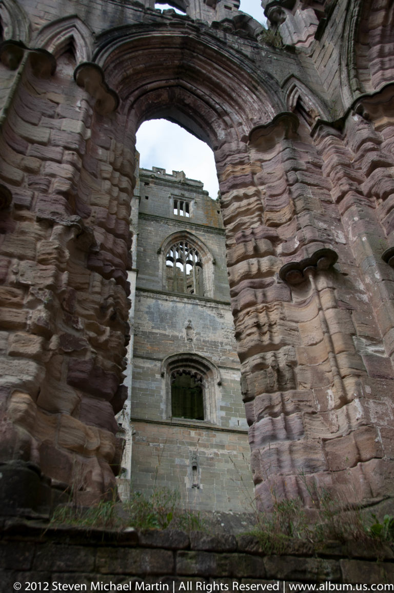 A pale abbey range appears through a foreground stone arch.