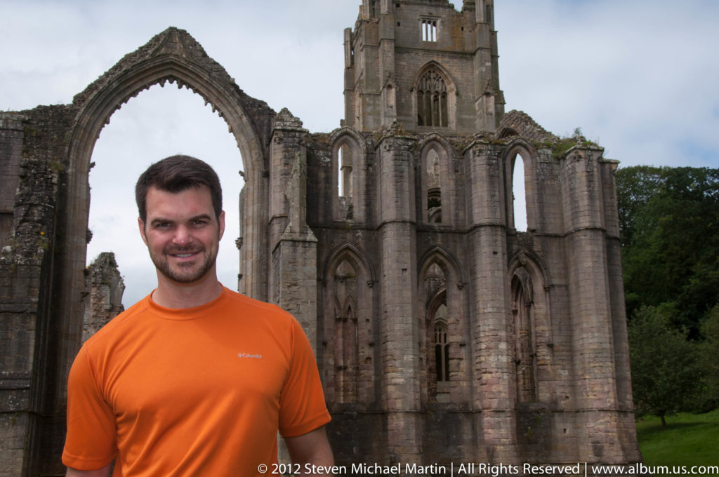 A visitor stands beside the tall roofless church walls at Fountains Abbey.