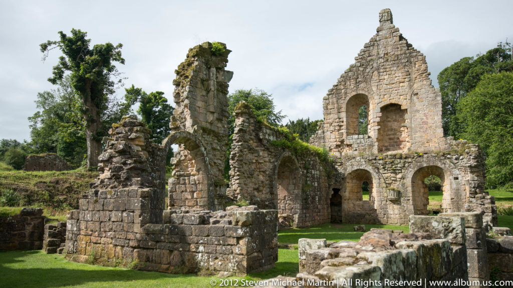 A central gable rises over arched openings and low foundations in the abbey ruins.
