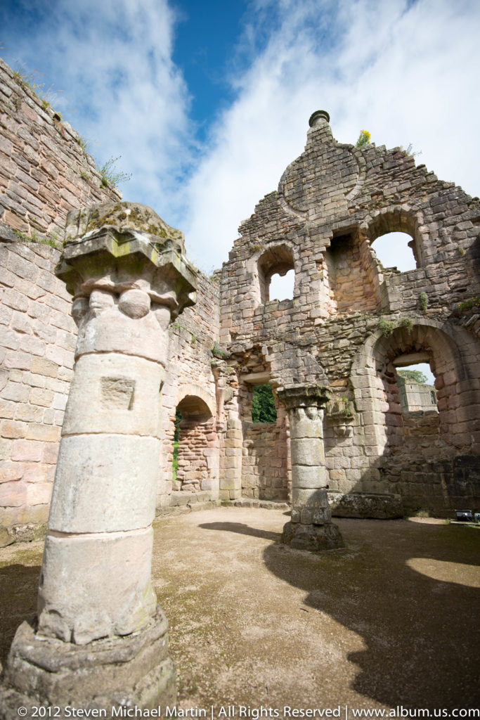 A stone fountain stands before a tall ruined abbey building.