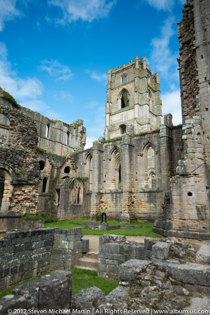 The roofless abbey church rises above the green precinct and low foundations.