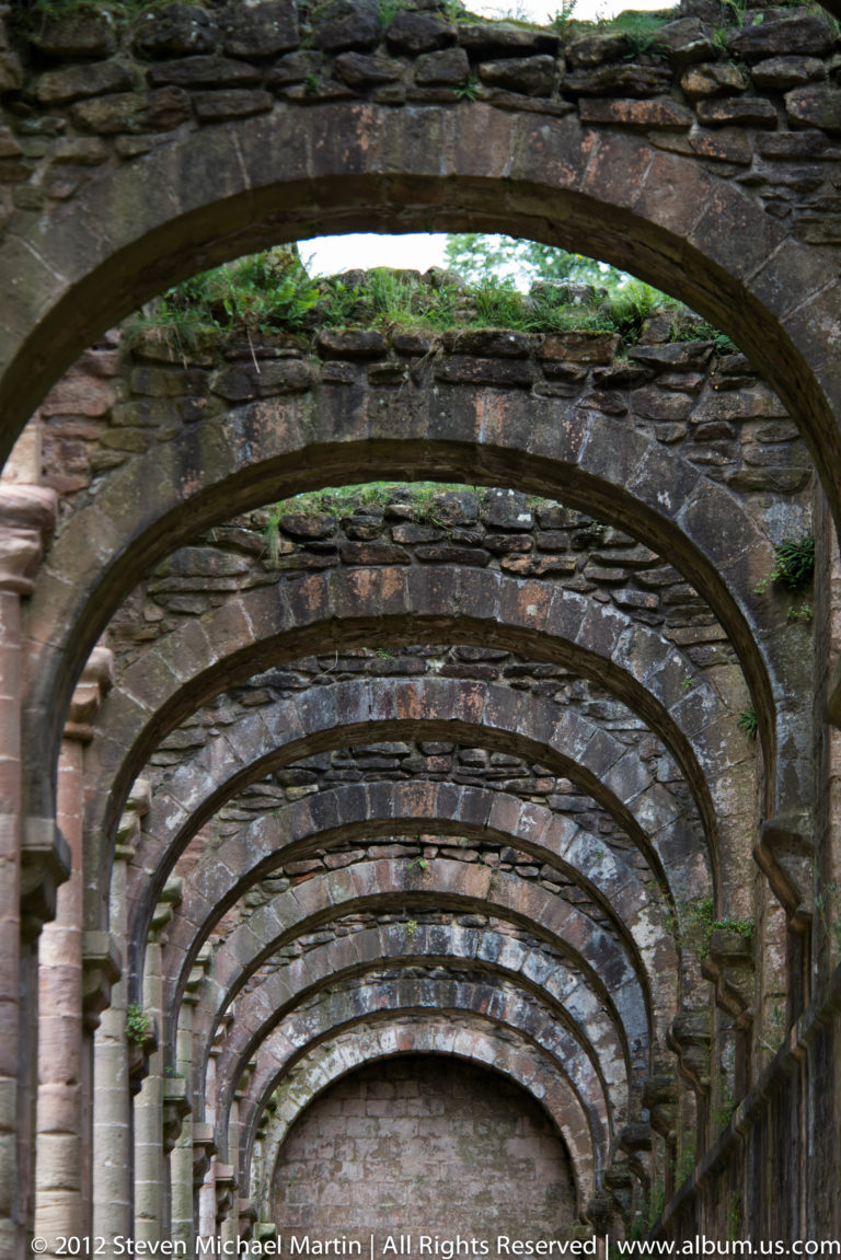 Nested stone arches form a deep perspective through a covered abbey passage.