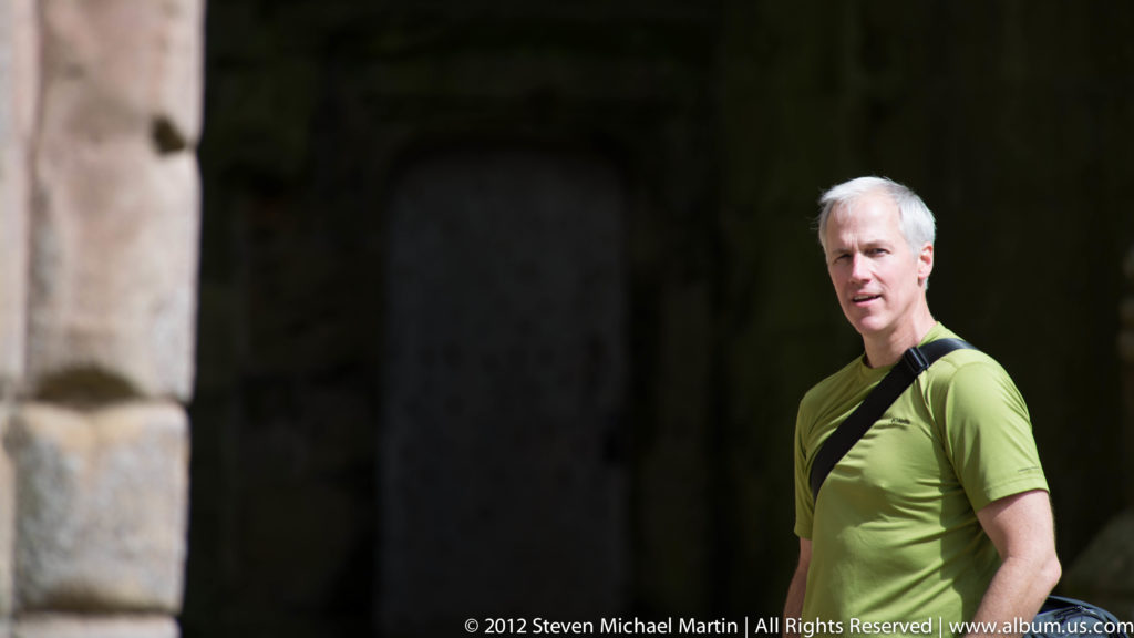 A visitor stands beside a dark stone arch at Fountains Abbey.
