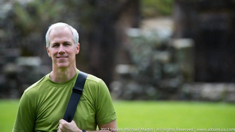 A white-haired man in a green shirt poses against a blurred background.