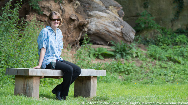 A visitor sits on a bench beside a low opening in a stone abbey wall.