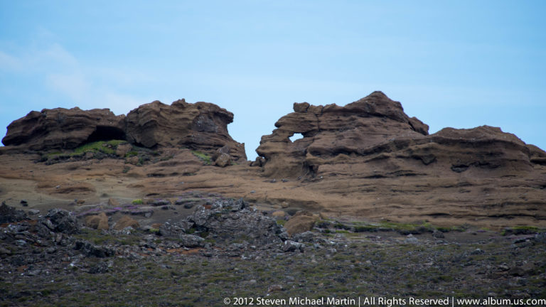 Dyrhólaey’s basalt sea arch opens beneath the headland with offshore rock stacks beyond.