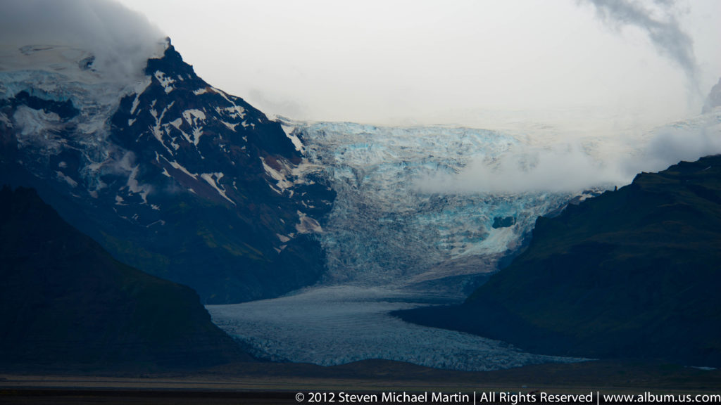 Breiðamerkurjökull descends between dark slopes beyond the waters of Jökulsárlón glacier lagoon.