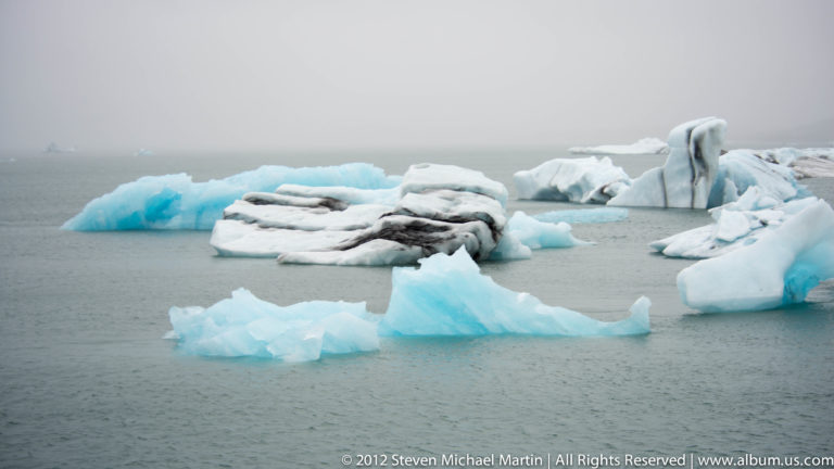White and blue icebergs float across Jökulsárlón glacier lagoon beneath a low gray horizon.