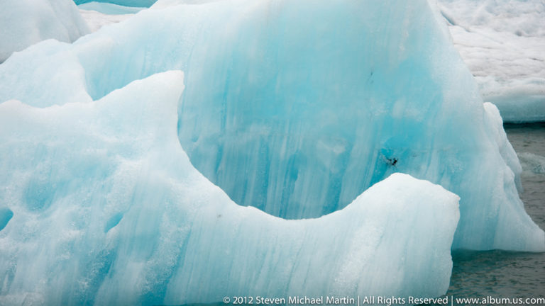 Close view of a blue iceberg with a dark diagonal fissure floating in Jökulsárlón glacier lagoon.