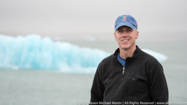 A traveler in a blue cap stands before icebergs floating across Jökulsárlón glacier lagoon.