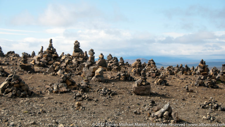 Many small stone cairns cover a rocky plain, with a taller stack near the center.