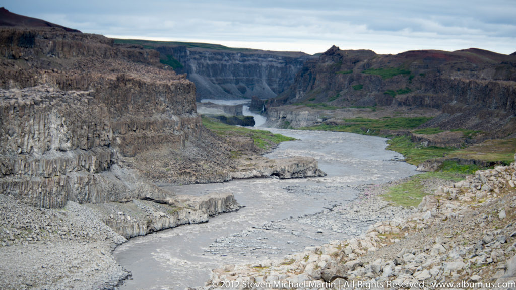 A pale river curves through a deep gorge beneath long, flat-topped basalt cliffs.