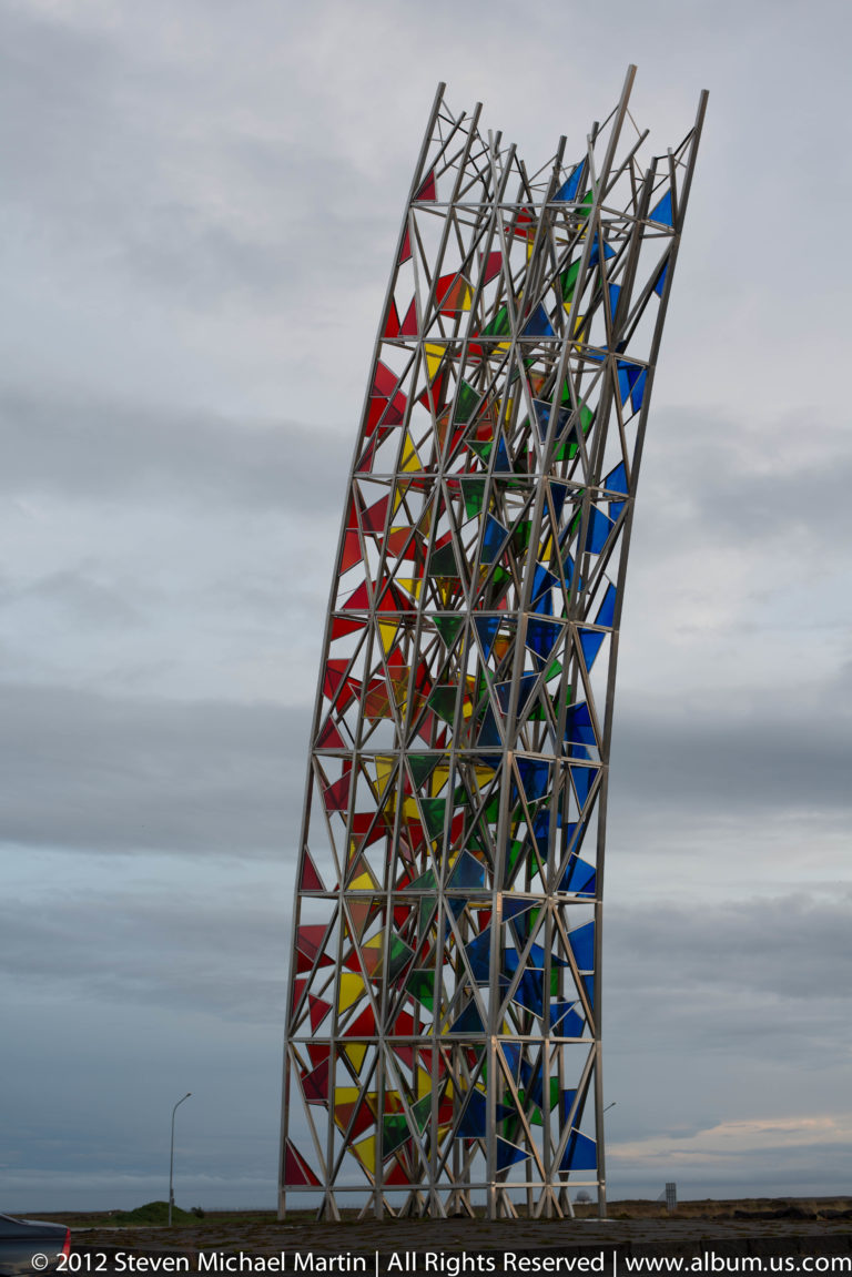 A tall steel lattice tower with colorful panels rises against a gray sky.