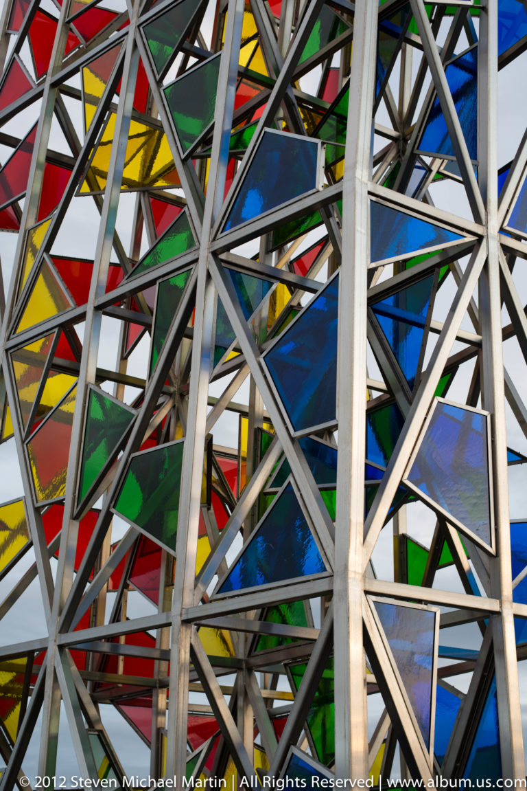 Close-up of pale steel cross-bracing over red, blue, yellow, and green glass panels.