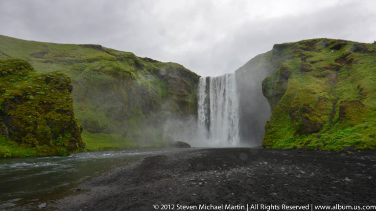 Gljúfrabúi waterfall descends through a narrow dark cleft beneath a green cliff rim.